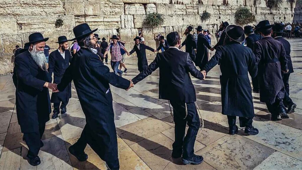 Group of Orthodox Jews dances next to ancient limestone wall known as Wailing Wall in the Old City of Jerusalem